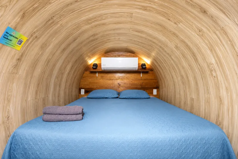 A bed inside a wood-lined cylinder room at Arenal Secret Garden