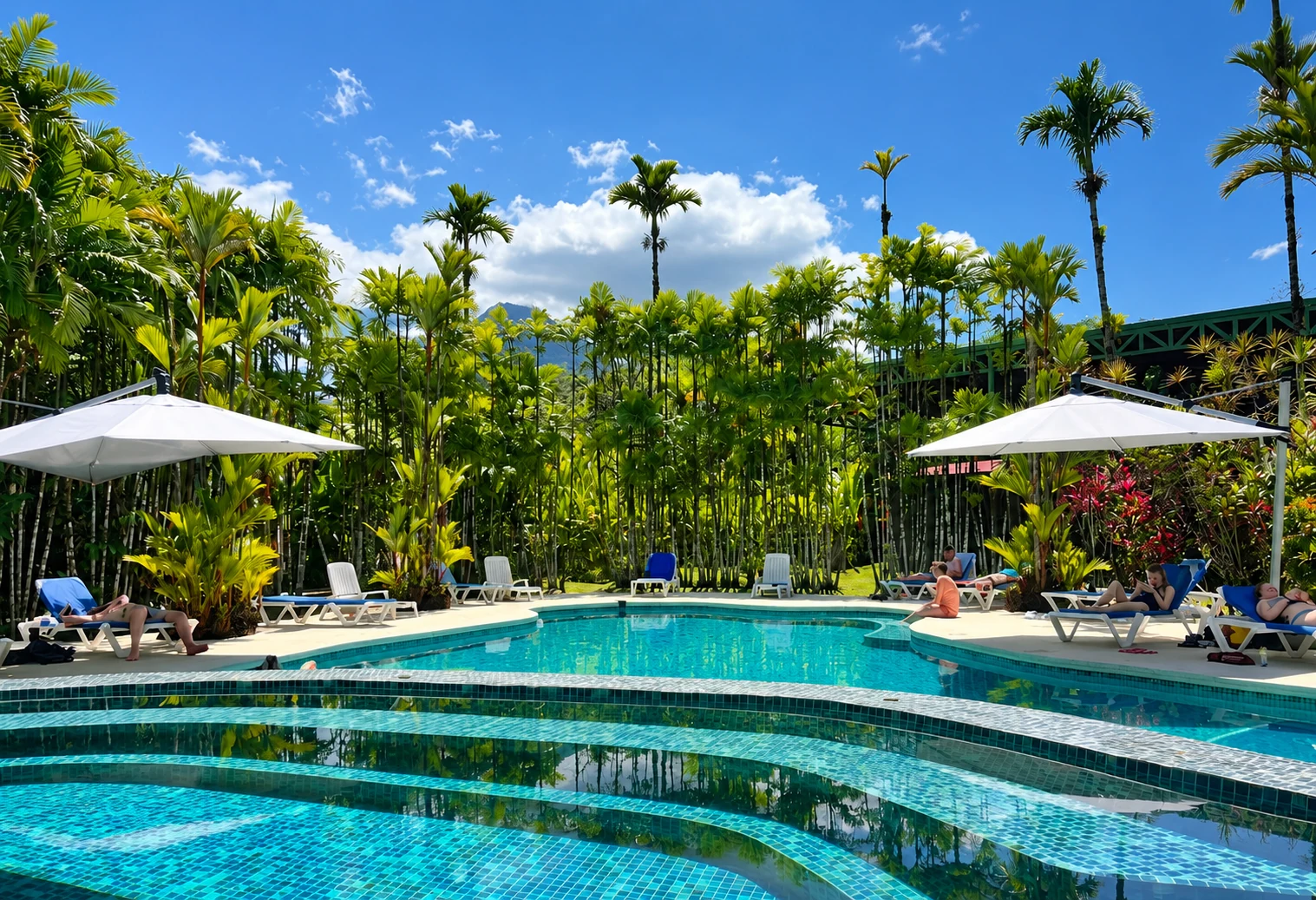 The Arenal Backpackers pool with white parasols, turquoise water and tropical palms